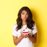 imagem de mulher afro americana indecisa e triste parecendo chateada nao consegue comer bolo em pe sobre fundo amarelo